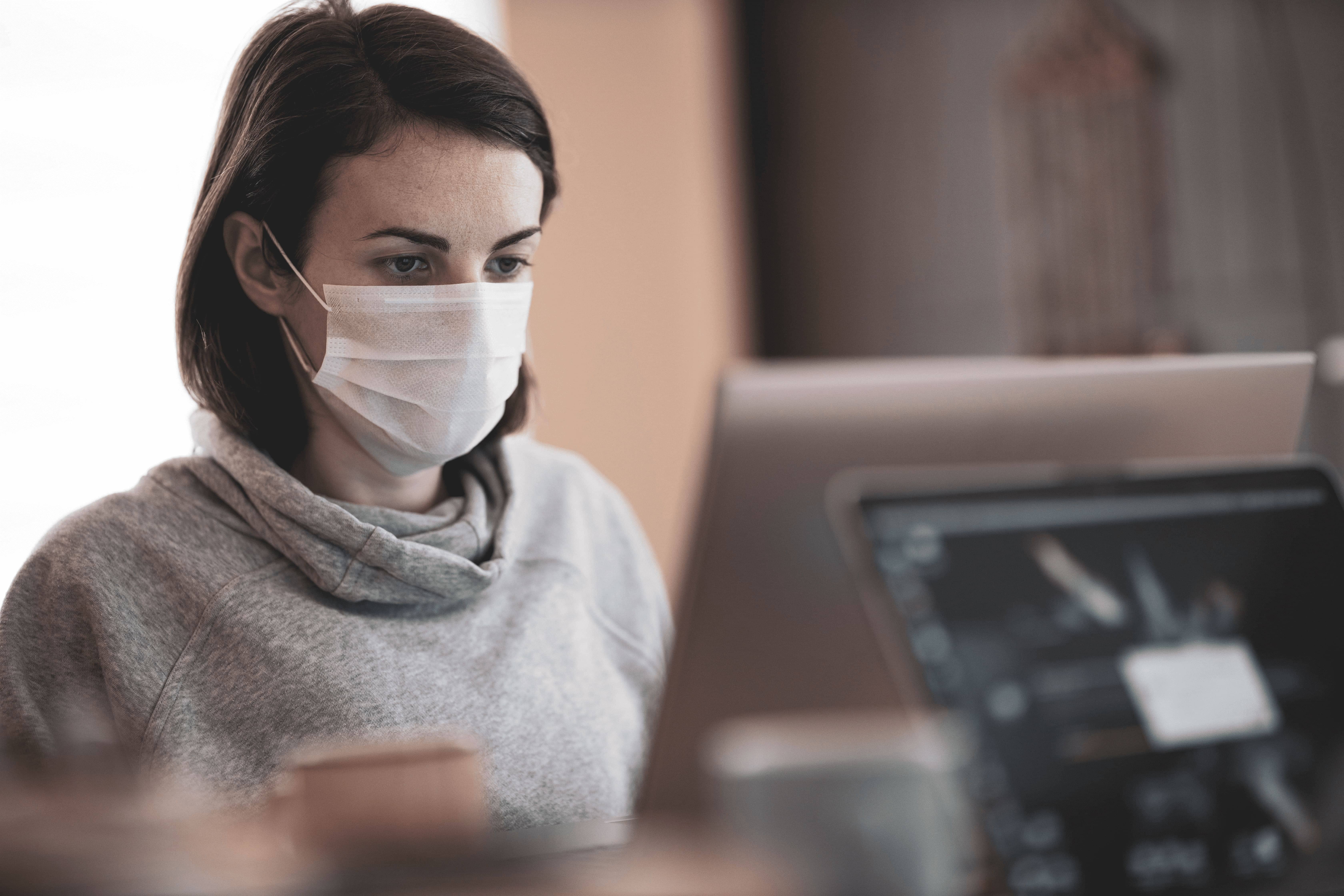 Frau mit der Maske sitzt am Computer